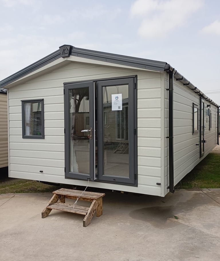 Modern mobile home con exterior crema y acabado oscuro, grandes ventanas y puertas dobles, con escalones de madera